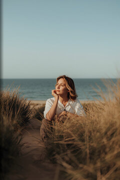 Woman sitting on a dune journaling with sea behind her evoking reflective slow living mood generative AI
