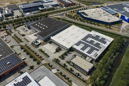 Aerial view of an industrial park with large warehouses, solar panel installations on rooftops, parking areas, and surrounding green spaces in the Netherlands.