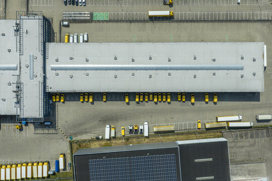 Aerial view of the DHL logistics facility with yellow delivery trucks parked at loading docks and solar panels on the adjacent building in Zwolle, Overijssel, Netherlands.