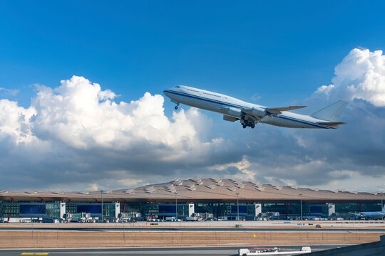White airplane climbs into the sky over a modern terminal building at the airport during the afternoon hours under a clear blue sky