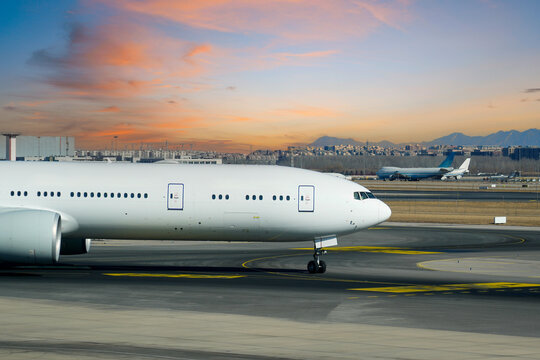 Large commercial jet travels along the airport tarmac at twilight while another plane waits in the background under a colorful evening sky