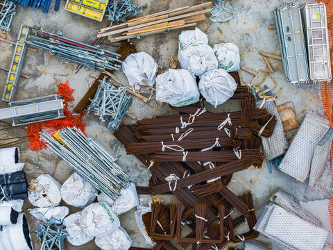 Aerial view of construction materials including stacked rebar, scaffolding components, and white supply bags at a construction site in Serravalle Scrivia, Piedmont, Italy.