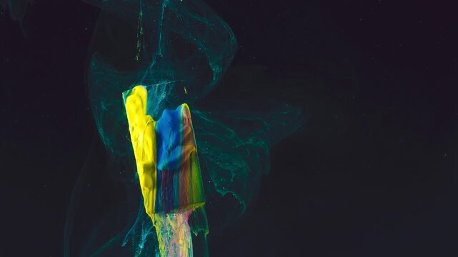 Close-up of paint-coated sponge brushes creating glossy multicolor trail with teal ink plumes against dark background