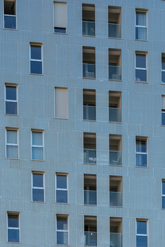 Under even daylight, blue tones settle over a minimal apartment facade, where repetition organizes windows and balconies across Nordbahnviertel, Vienna, Austria.