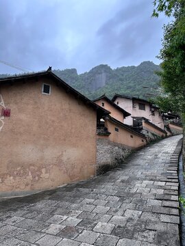 Cobblestone pathway leading up through historic traditional Chinese village with rammed earth walls and mountain backdrop