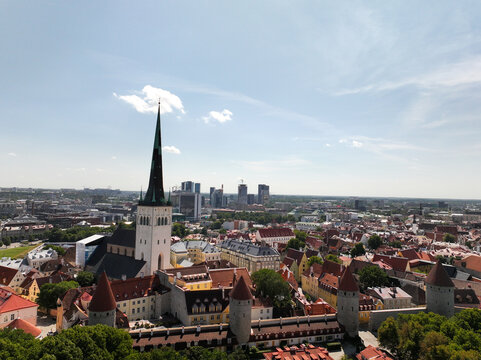 Aerial view of St. Olaf's Church spire rising above the historic rooftops, medieval defensive towers, and the modern skyline of Tallinn, Harju County, Estonia.