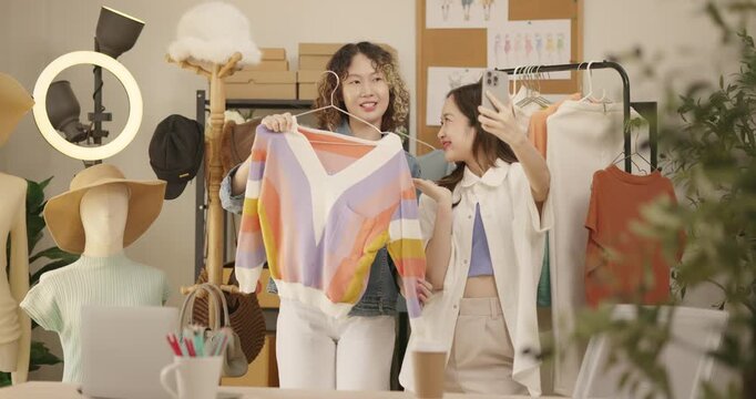 Asian woman influencer live streams a fashion product showcase from studio. Two female SME Online store business owner selling clothes on social media. entrepreneur, e-commerce, side hustle concept.