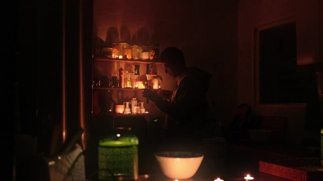 Silhouette of a man lighting candles on shelves in a dark kitchen, creating a warm, cozy, and magical atmosphere for a relaxing evening and intimate moment at home during a power outage