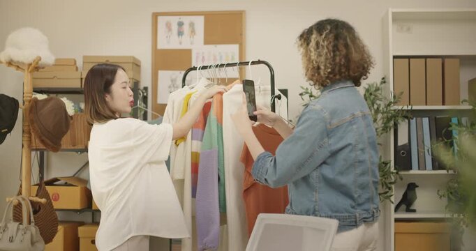 Asian woman influencer live streams a fashion product showcase from studio. Two female SME Online store business owner selling clothes on social media. entrepreneur, e-commerce, side hustle concept.