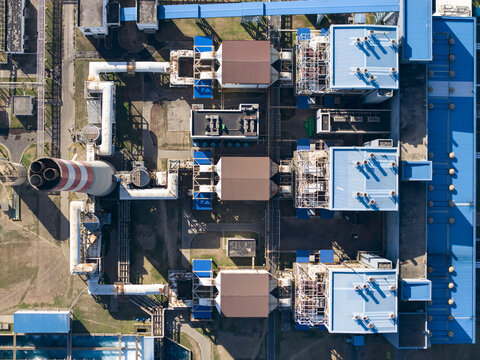 Aerial view of Celukan Bawang Steam Power Plant with industrial structures, blue rooftops, and a tall chimney stack in Buleleng, Bali, Indonesia.