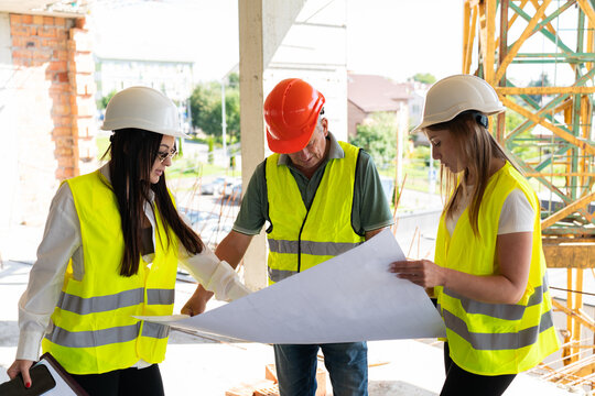 Contractor and female inspectors examine object blueprint. Lady engineer and worker look at sheet with room layout standing on high floor
