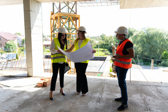 Female inspectors and builder examine unfinished real estate plan. Worker and engineers compare blueprint with results of professional actions