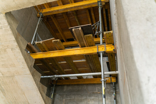 Ceiling formwork with yellow beams and metal props stands under concrete span of building shell. Structure supports load and holds panels