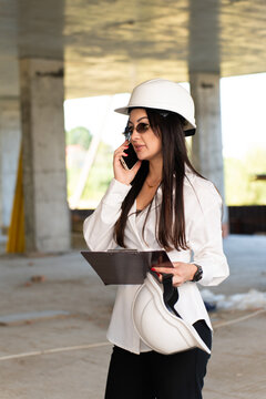 Female engineer talk on smartphone standing on construction site. Woman informs management about inspection results and building status