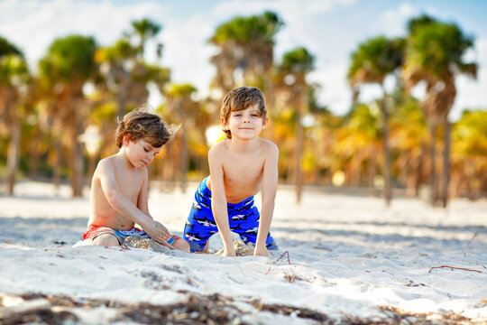 Two little kids boys having fun on tropical beach, happy best friends playing with sand, friendship concept. Siblings brothers in swim trousers. Key Biscayne, Miami, Florida