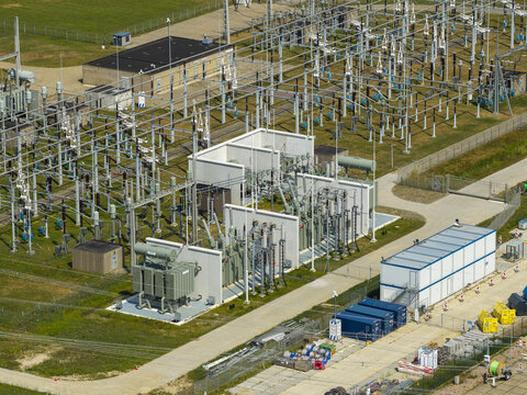Aerial view of an electrical substation featuring high-voltage transformers, switchgear, and metal structures within a fenced facility in the Netherlands.