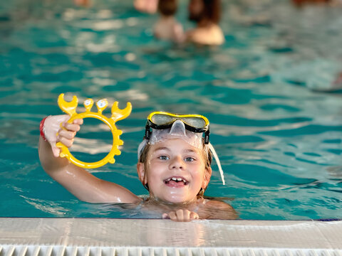 Happy little girl with in swimming pool learning to dive. Little school child with swimm glasses, picking things from pool bottom. Healthy sport activity and fun for children.