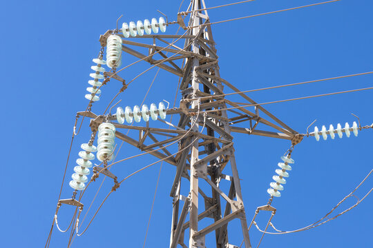 High voltage power line tower with glass insulators against a clear blue sky