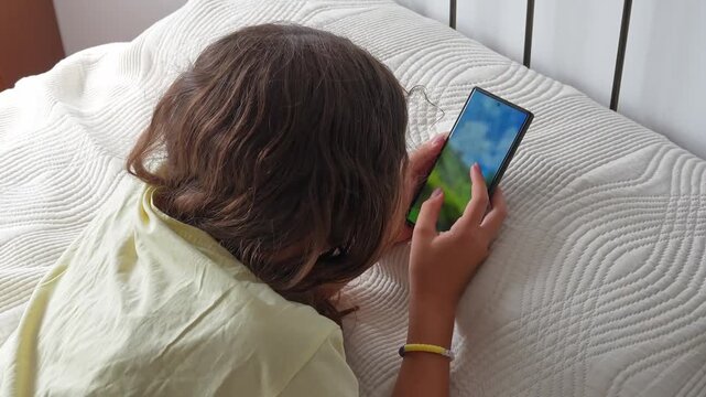 young girl lying in bed and using a smartphone. She is zooming in on an image on her mobile phone during her screen time