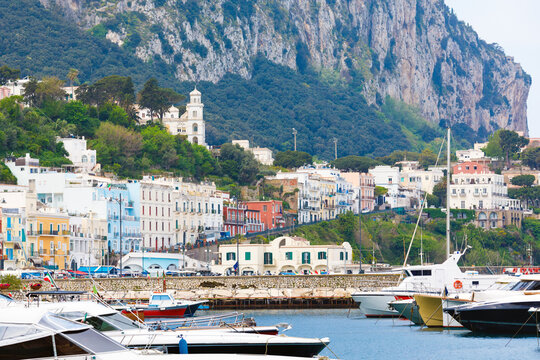 Capri rises above yachts, harbor, church, and Mediterranean shoreline under soft daylight with calm coastal atmosphere. Welcome to Capri, Italy concept image