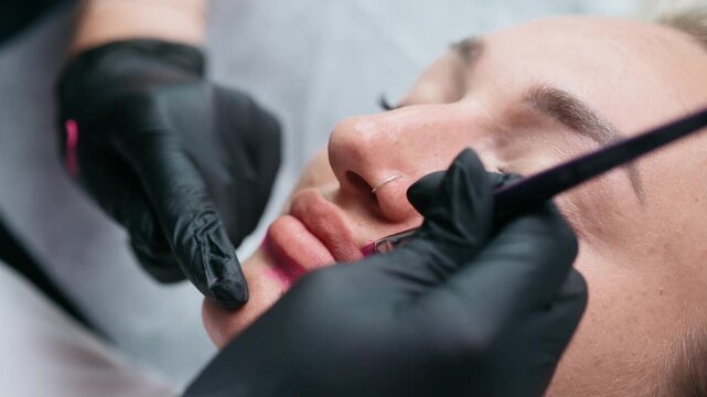 Permanent makeup artist maps lip contours with cosmetic pigment before a lip blush tattoo procedure in a professional beauty salon.