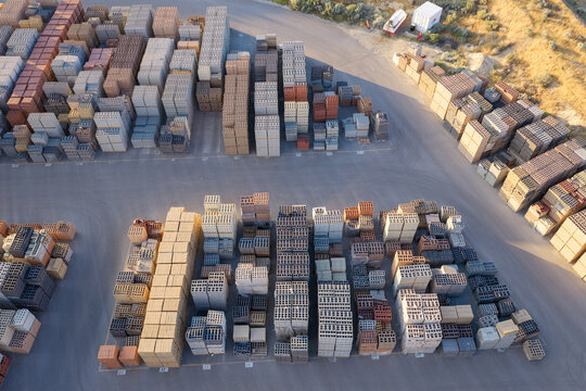Aerial view of organized stacks of construction materials including bricks, pavers, and cinder blocks arranged in rows on a paved yard in Bluffdale, Utah, United States.