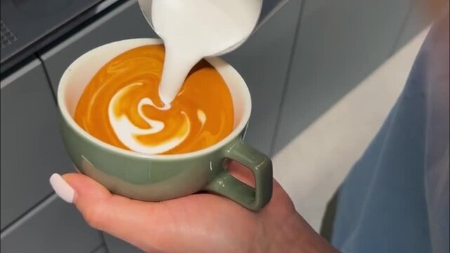 Barista Pouring Steamed Milk to Create Latte Art Rosetta Pattern in Green Coffee Cup