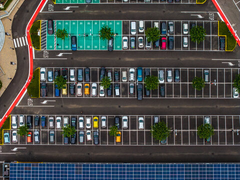 Aerial view of the Designer Outlet Serravalle parking lot with rows of parked cars, green designated spaces, and solar panels in Serravalle Scrivia, Piemonte, Italy.