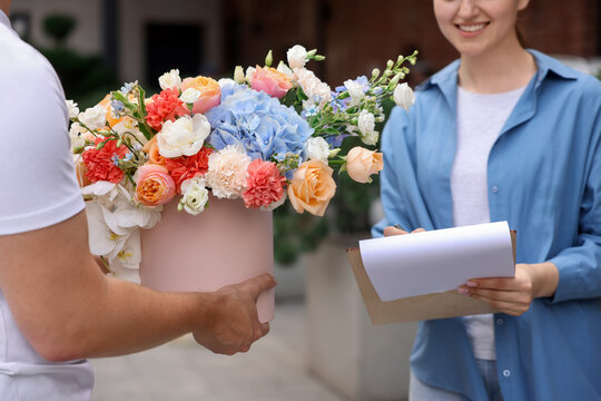 Courier giving beautiful bouquet of flowers to woman outdoors, closeup. Client signing paperwork