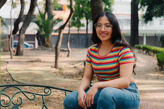Smiling young woman with glasses sitting on a green park bench