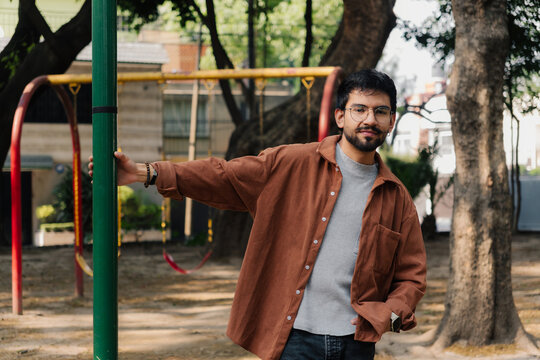 Smiling young man with beard and glasses standing in a park