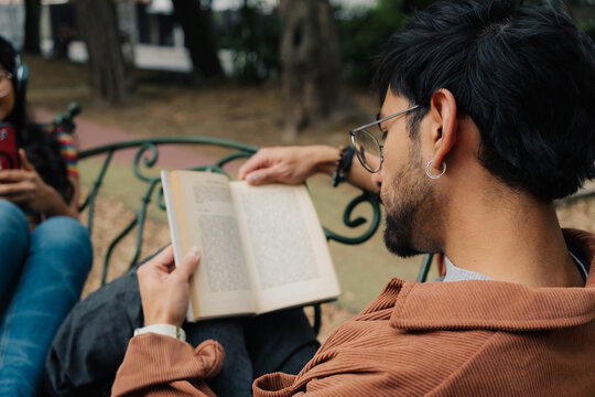 Young man reading book on park bench during a sunny afternoon