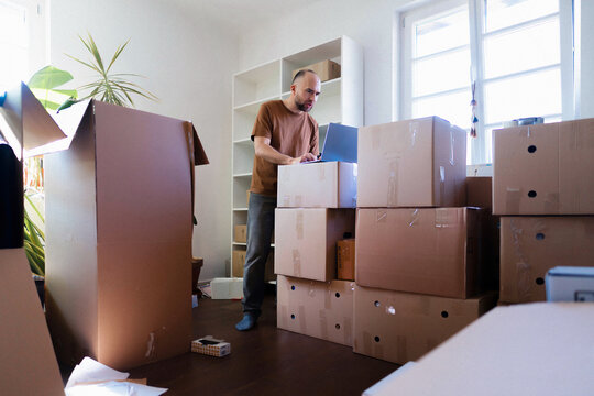 Man Working on Laptop Amid Moving Boxes in Apartment