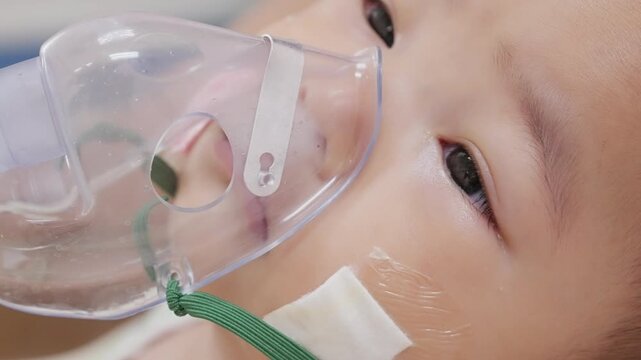 Infant boy wears a nebulizer mask during asthma treatment at hospital, illustrating pediatric respiratory healthcare, inhalation therapy, breathing support, and medical care.
