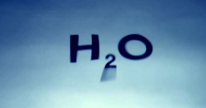 Conceptual studio video featuring the word "H2O" printed in blue on a white background and filmed through a wavy water surface that creates natural optical distortion. 