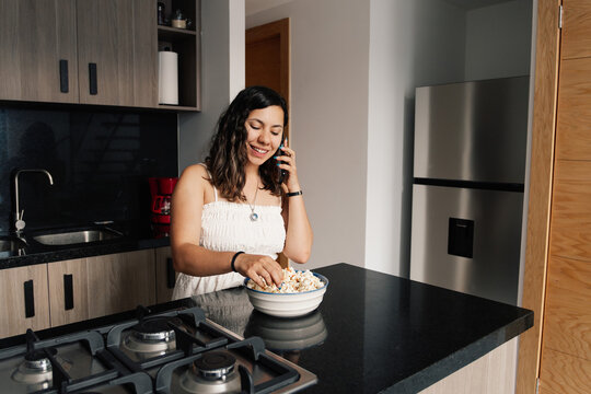 Woman in the kitchen talking on the phone and eating popcorn