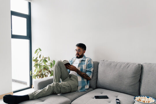 Young man reading relaxed on a sofa with snacks