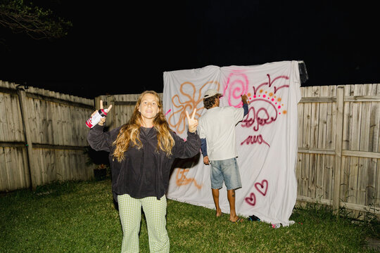 Friends spray painting graffiti sheet at backyard party