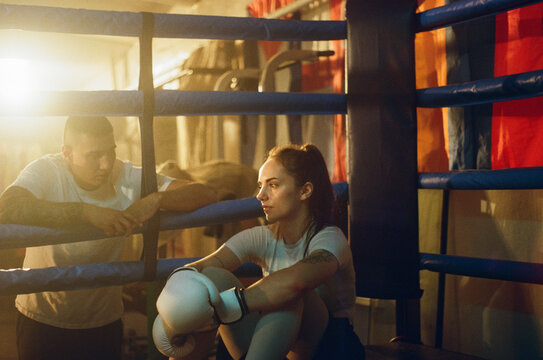 Female boxer listens to trainer in boxing ring during the break. 