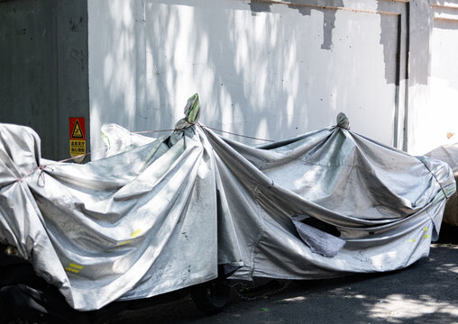 Motorbikes covered in white tarps on city street during the day