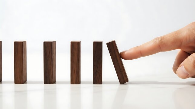 Finger pushing a wooden domino block to start a chain reaction