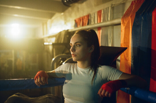 Female boxer rests leaning on ropes in ring corner