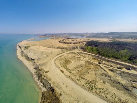 Aerial view of a large-scale mining and landfill site along the Black Sea coast with heavy trucks, dirt roads, and excavated earth in Istanbul, Turkey.