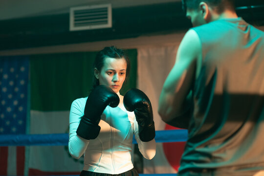 Boxer woman trains with coach in boxing gym.