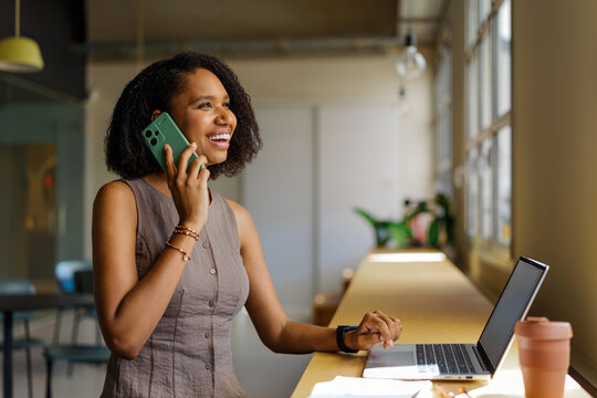 Woman smiling while using phone and laptop at workspace
