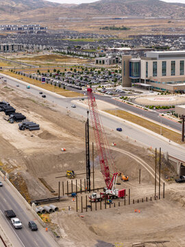 Aerial view of the 2100 North Freeway construction project with a large red drilling rig crane, heavy machinery, and steel beams in Lehi, Utah, United States.