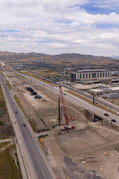 Aerial view of the 2100 North Freeway construction project featuring a large red crawler crane, heavy machinery, and ongoing road work near a hospital in Lehi, Utah, United States.