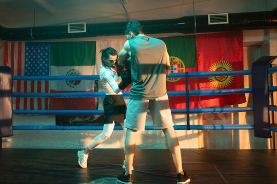 Female boxer strikes trainer holds mitt pads with uppercut in the ring