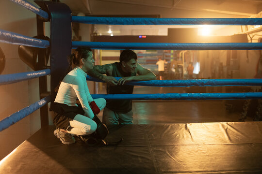 Woman boxer resting between fight round near trainer in  boxing ring.