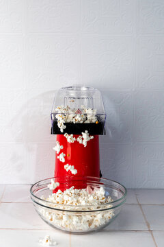 Red air popcorn popper, popping popcorn into a clear glass bowl in a white tile surface 